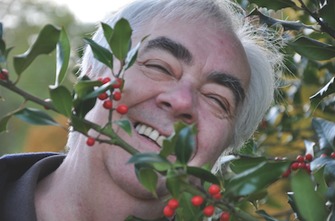 Author Claude Ponti smiles from behind a branch with green leaves and red berries