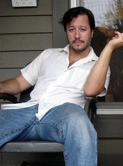 Illustrator Dean Haspiel poses in a white button down and blue jeans for the camera on the front porch of a house