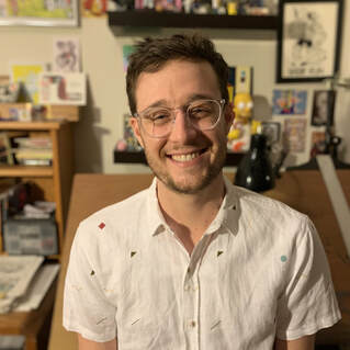 Author Ben Nadler smiles for the camera in a room crowded with art and knick-knacks 